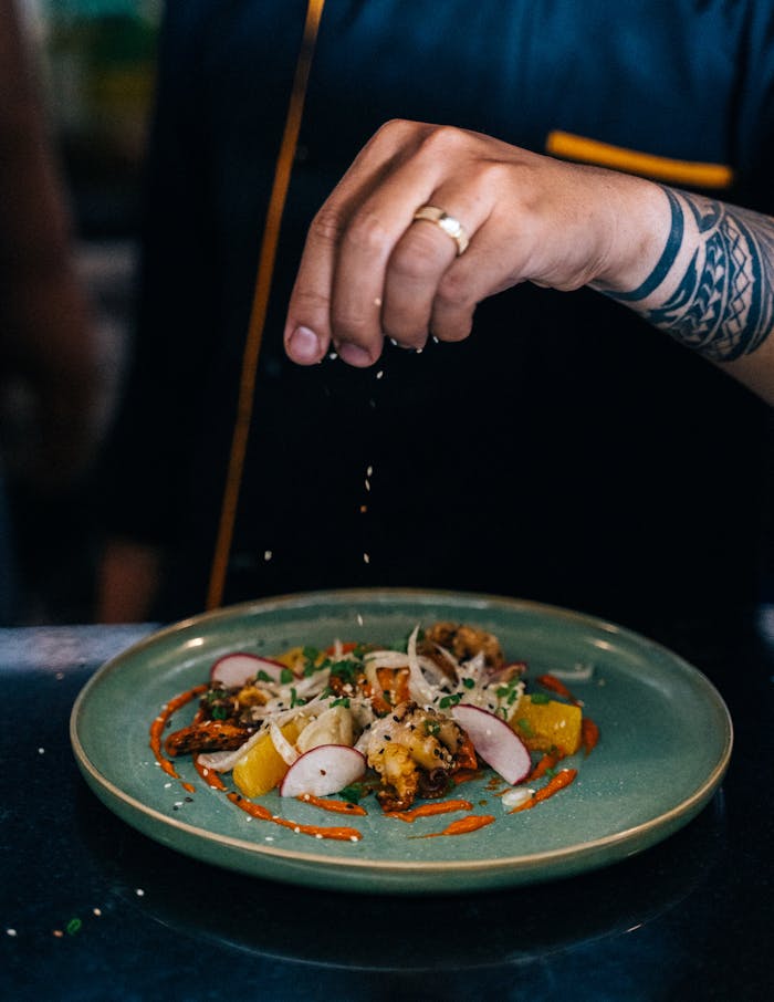 A chef adding final touches to a gourmet dish in an indoor restaurant kitchen.